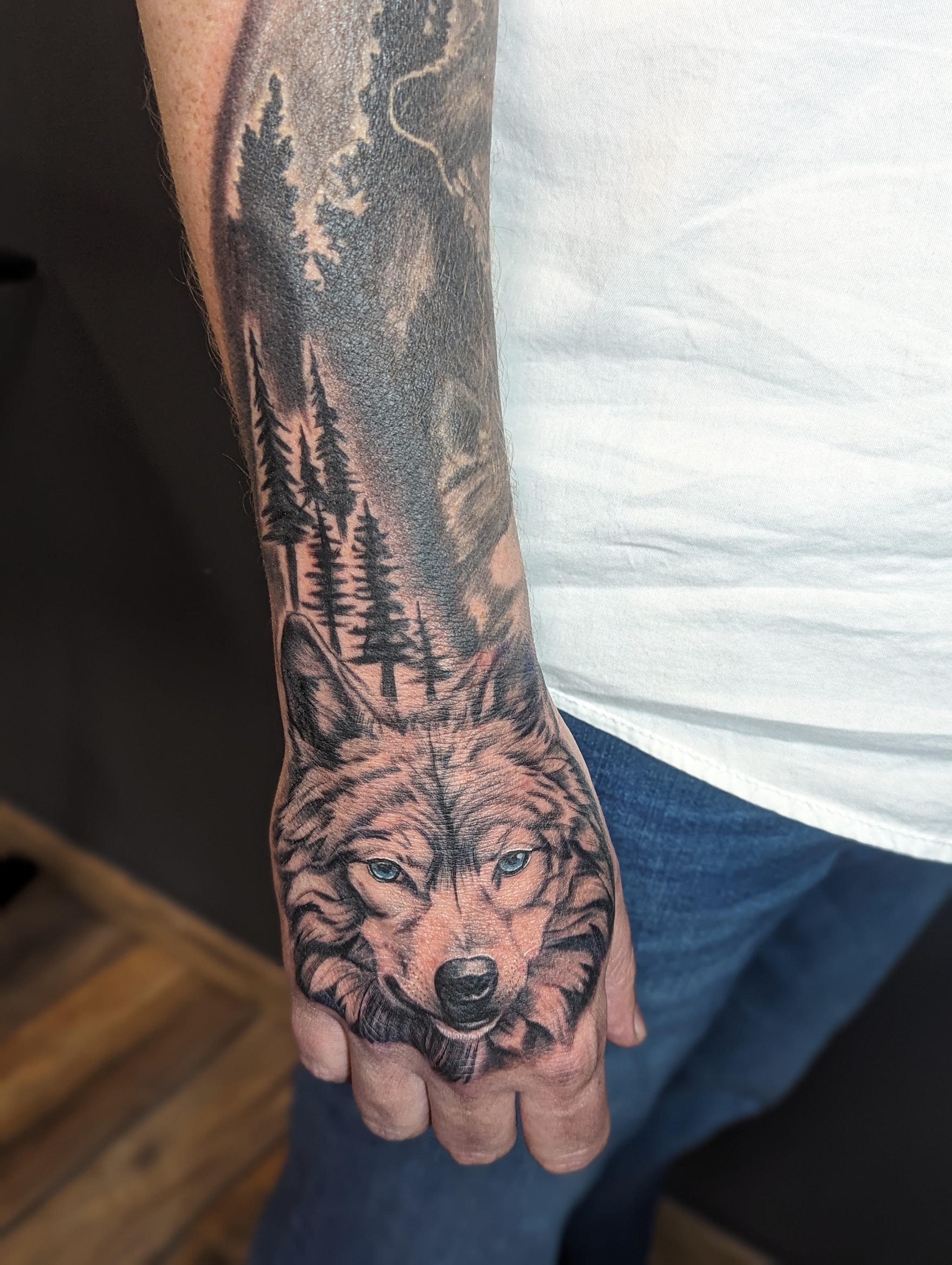 Realistischer Wolfskopf mit Waldmotiv am Unterarm und Handrücken